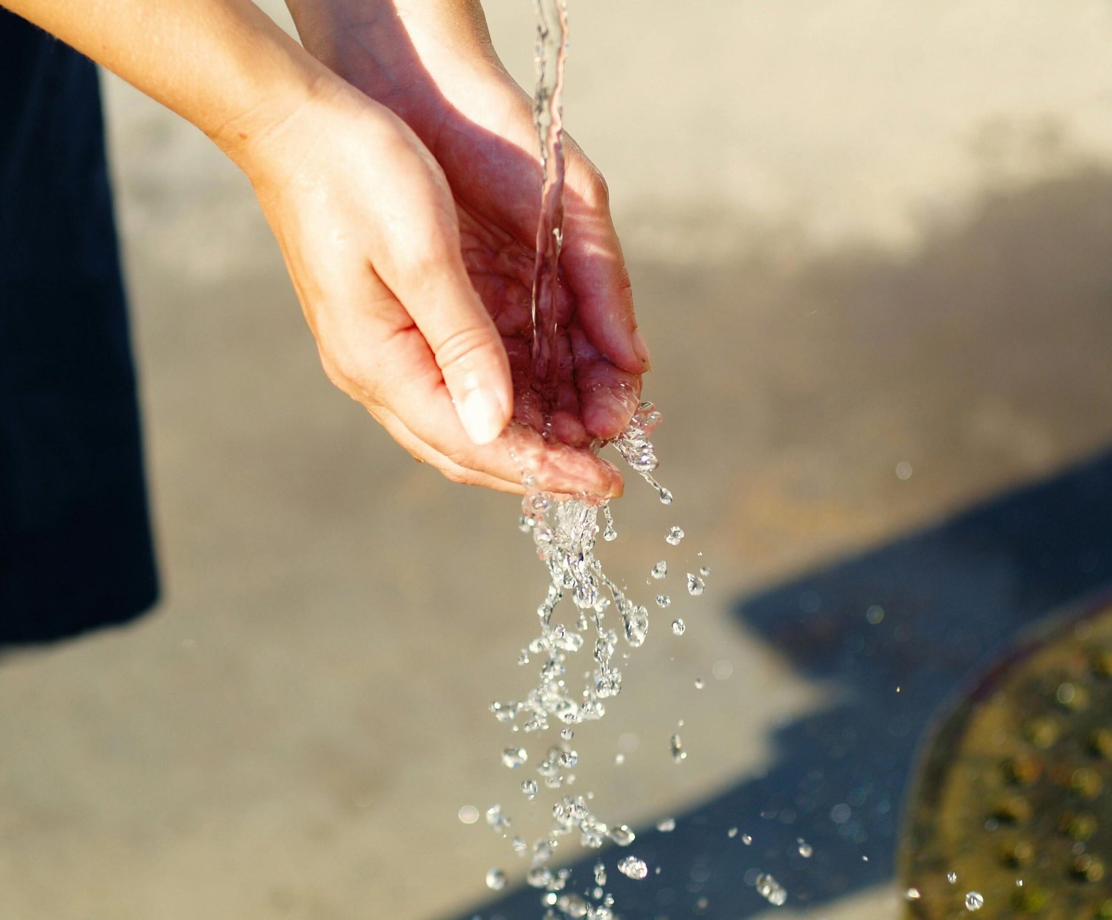 Close-up of hands catching flowing water outdoors, symbolizing freshness and purity.