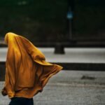 A woman walking in an outdoor setting with a flowing yellow hijab, capturing a dynamic street moment.