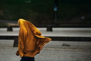 A woman walking in an outdoor setting with a flowing yellow hijab, capturing a dynamic street moment.